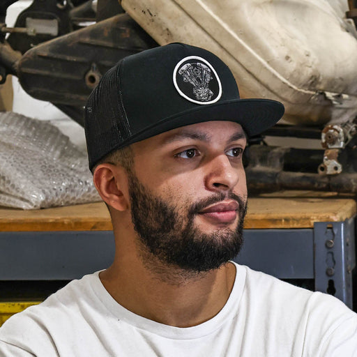 Man wearing a black cap with a logo in front of a vehicle