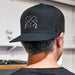 Person wearing a black cap with a logo, facing away from the camera.